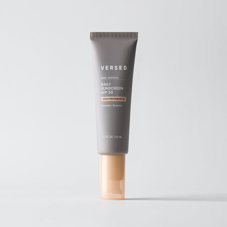 Gray tube of Versed Good Defense Daily Sunscreen SPF 50 with peach-colored cap on white background.